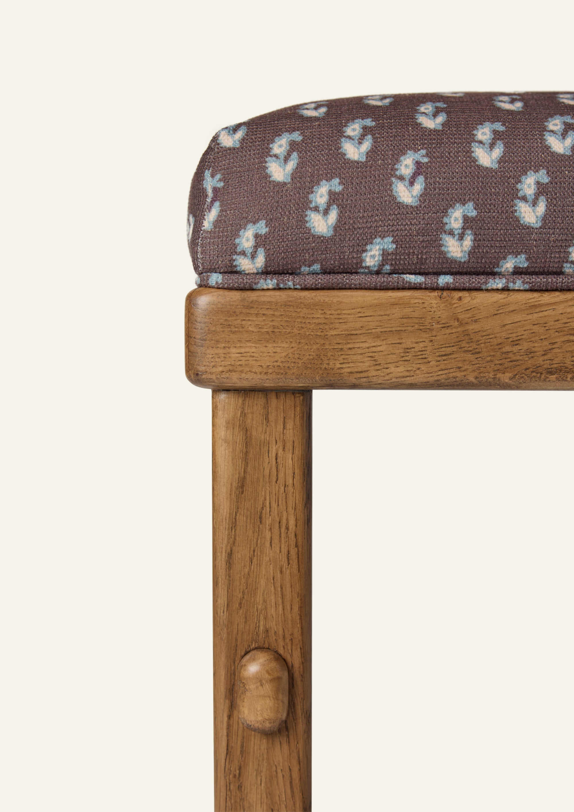 Close-up of the counter stool showcasing floral brown upholstery and a honey oak frame. The fabric features a small-scale floral print in soft blue and ivory against a rich brown ground.
