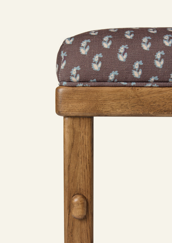 Close-up of the counter stool showcasing floral brown upholstery and a honey oak frame. The fabric features a small-scale floral print in soft blue and ivory against a rich brown ground.