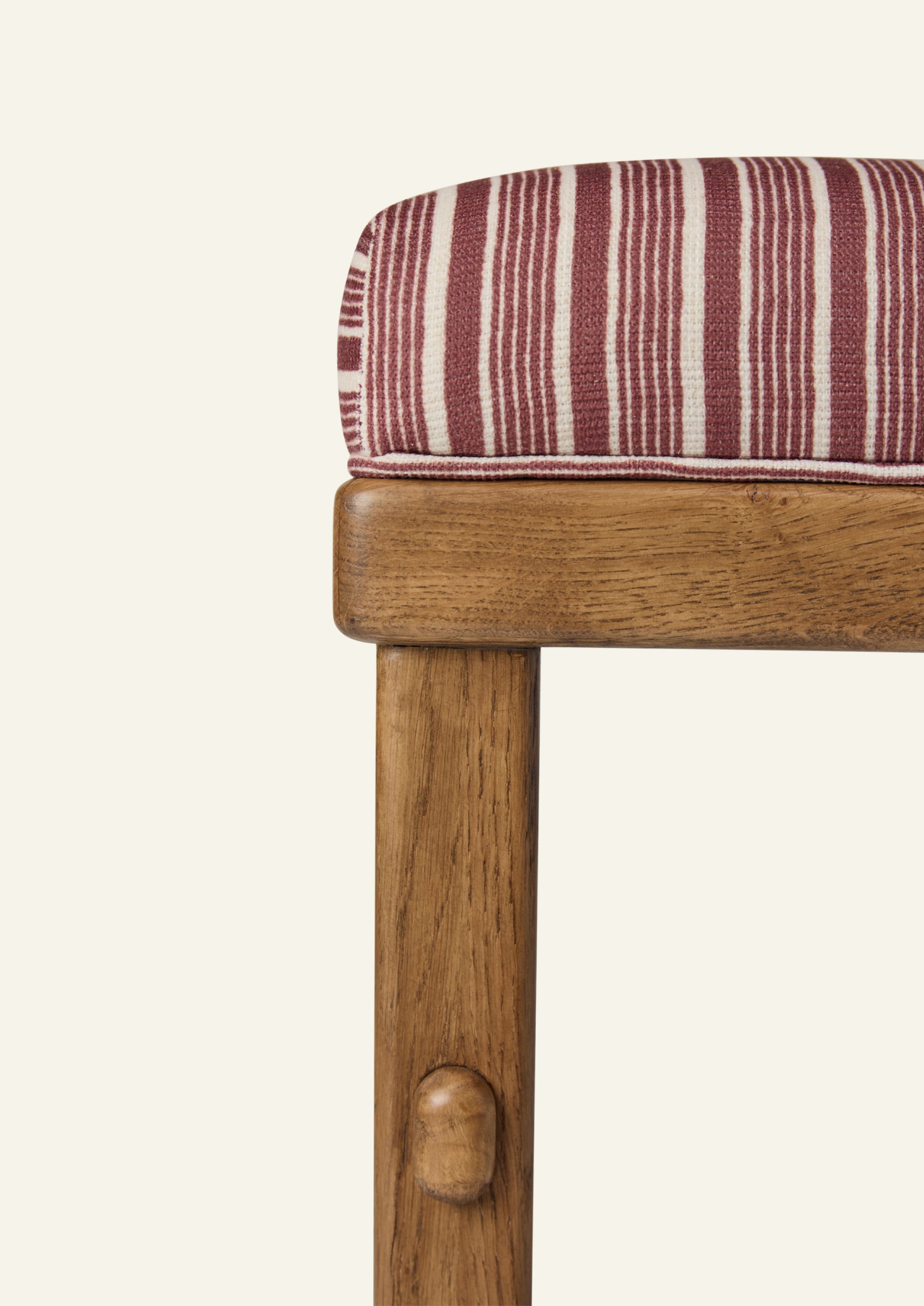 Close-up of the counter stool showcasing the Oxblood Stripe upholstery and honey oak frame. The woven fabric features burgundy-red stripes on a warm ivory ground, paired with handcrafted wood detailing.