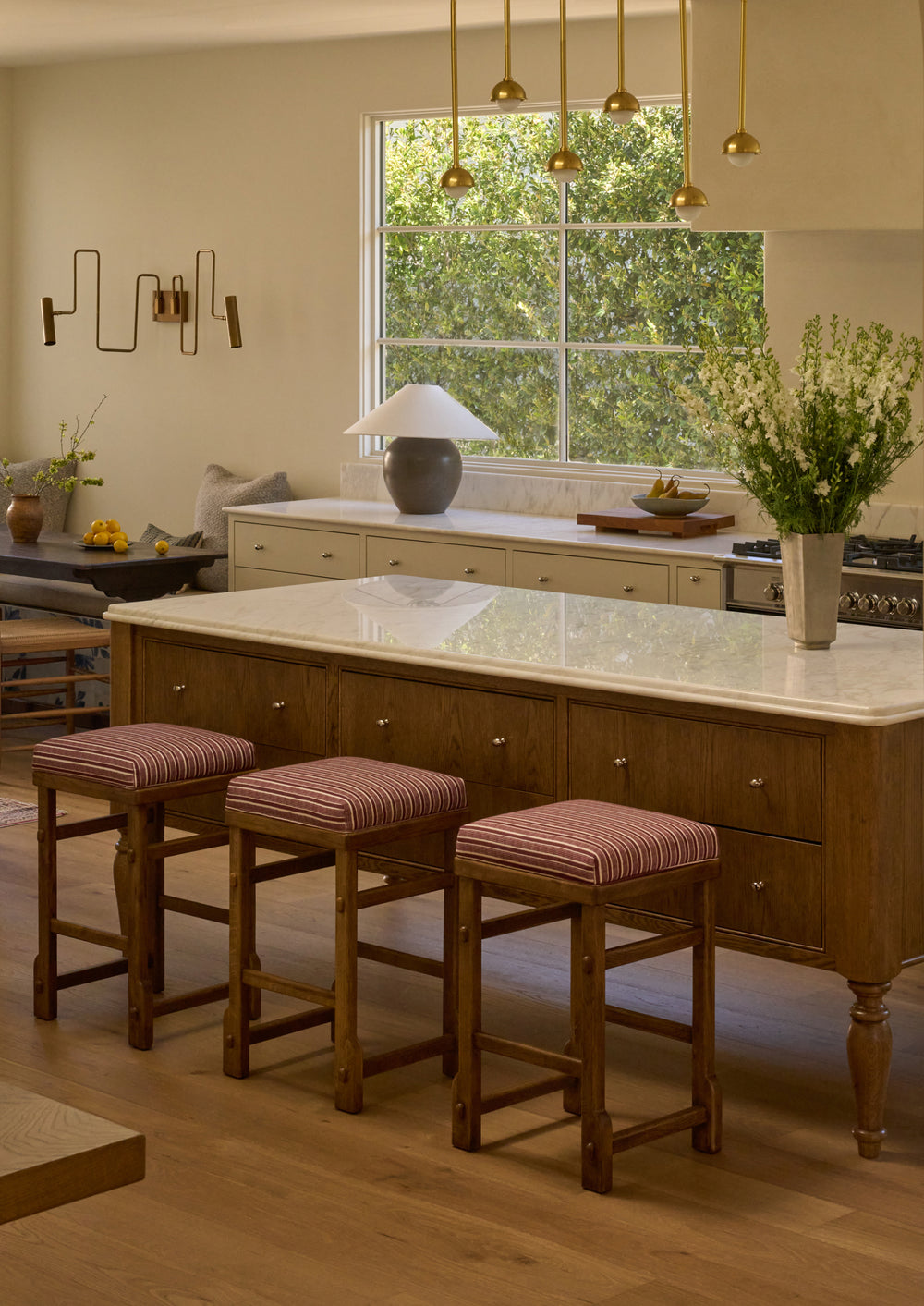 A set of upholstered counter stools in Oxblood Stripe are styled around a warm wood kitchen island with a marble countertop. The striped upholstery introduces color and pattern while complementing the rich wood tones throughout the space.