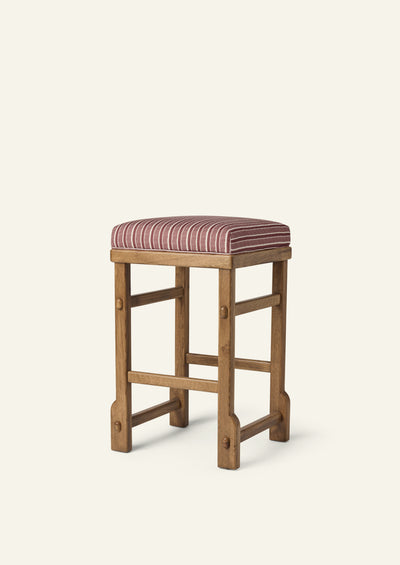Upholstered counter stool featuring a cushioned seat in Oxblood Stripe fabric atop a solid honey oak frame. Traditional exposed joinery details and a warm wood finish bring timeless character to the tailored silhouette.