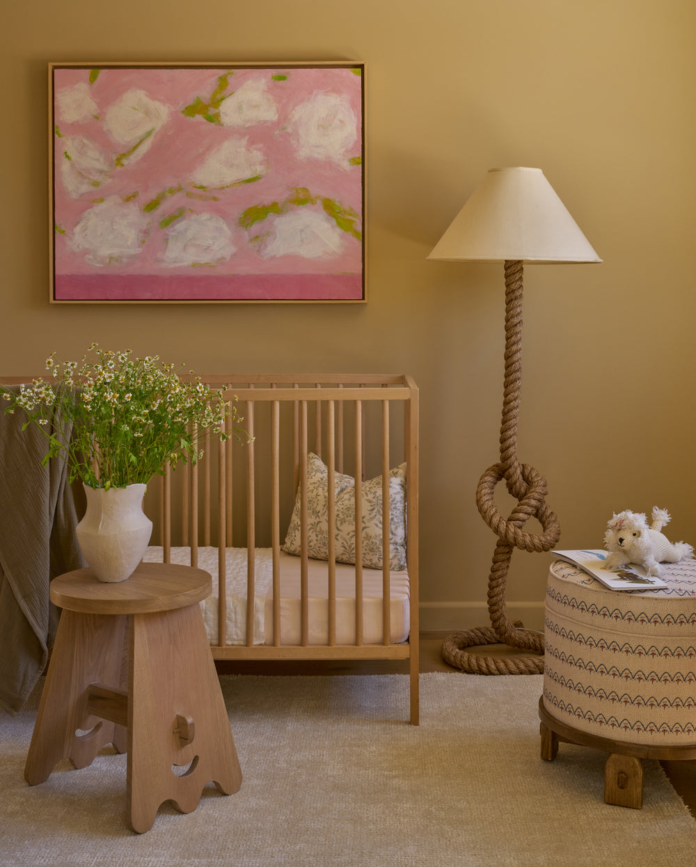 Nursery room with wooden crib, floral painting, and decorative lamp. The Senja is styled next to the crib with a vase of florals. 