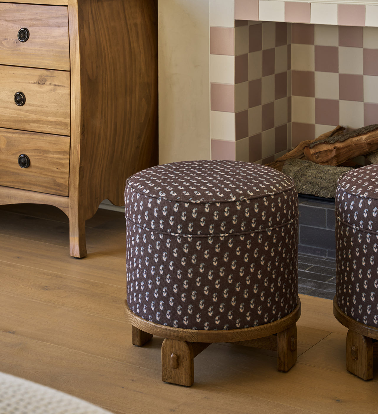 Round coco floral pattern Yara pouf with wooden base in a room with a fireplace and wooden dresser.