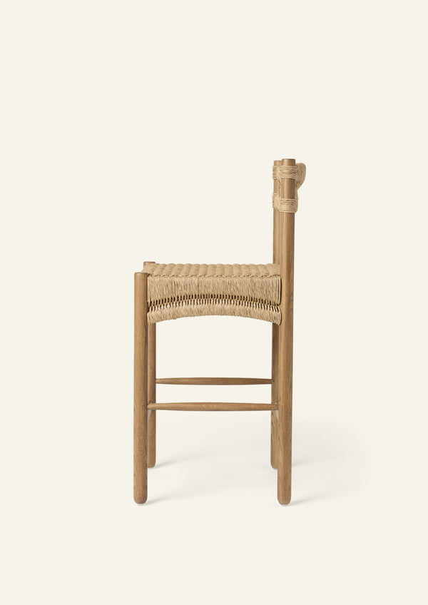 Side profile of the counter stool highlighting its woven seat, supportive backrest, and solid oak frame. The streamlined silhouette balances durability, comfort, and understated style.