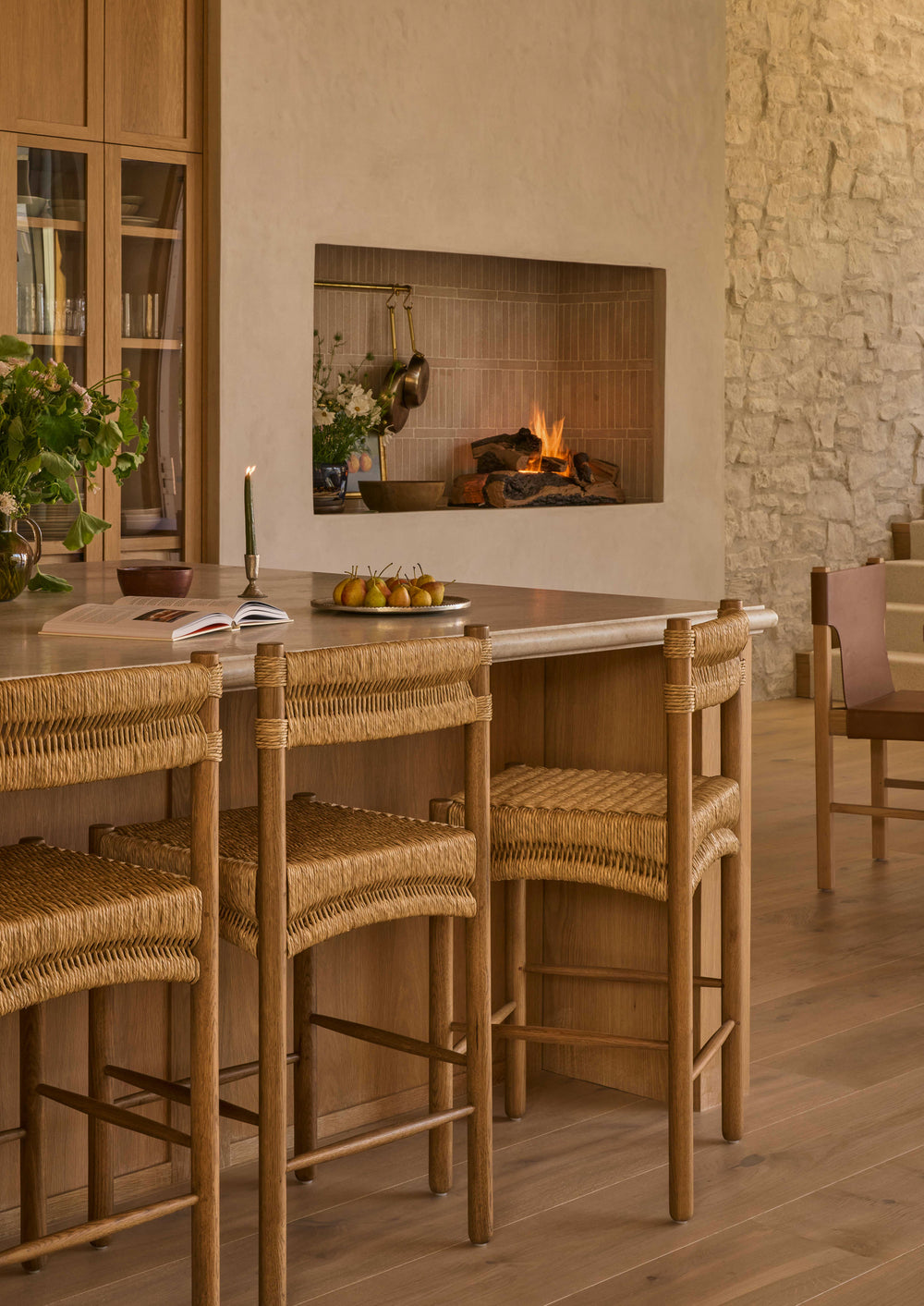 Counter stools styled around a large kitchen island in a warm, inviting interior. The woven rush and honey oak construction complement natural materials and relaxed, gathered living.