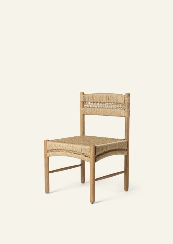 Three-quarter view of a dining chair crafted from solid honey oak and handwoven natural rush. The gently curved woven seat and wrapped backrest create a relaxed silhouette that blends coastal warmth with timeless craftsmanship.