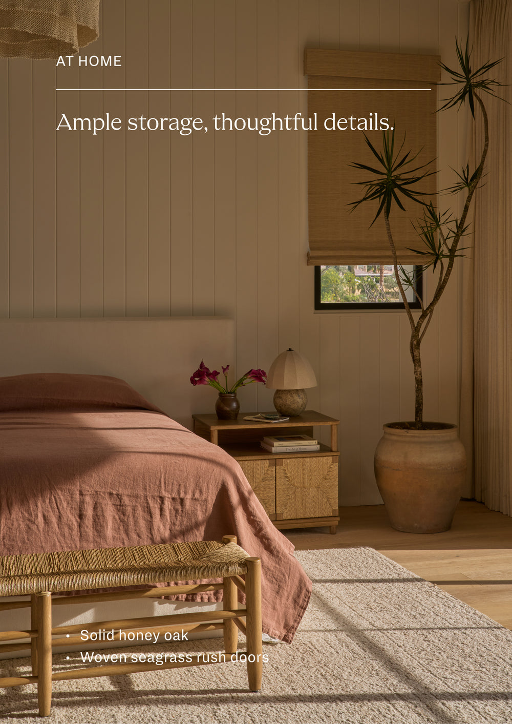 Ample storage, thoughtful details. Honey oak nightstand styled beside a bed in a warm, light-filled bedroom. The woven seagrass rush doors and open shelf create a functional storage solution with natural, organic appeal.