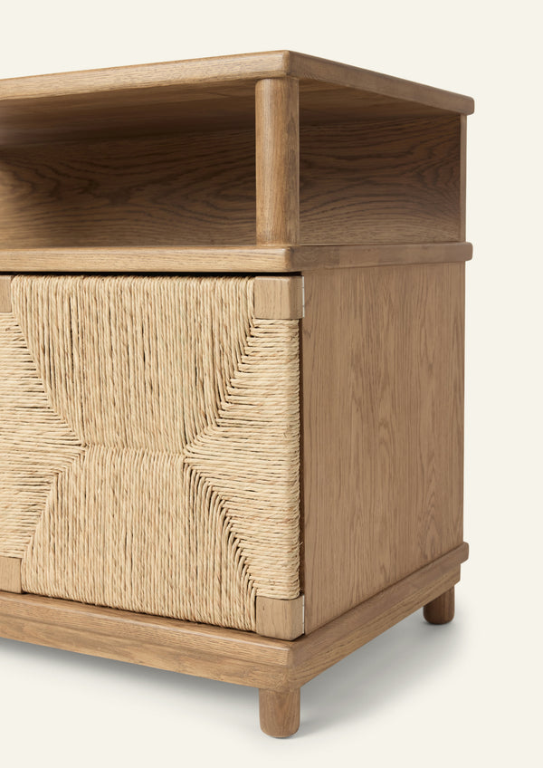 Close-up of the nightstand highlighting the woven seagrass rush door panel and solid oak frame. The geometric weave pattern showcases the natural texture and handcrafted character of the material.