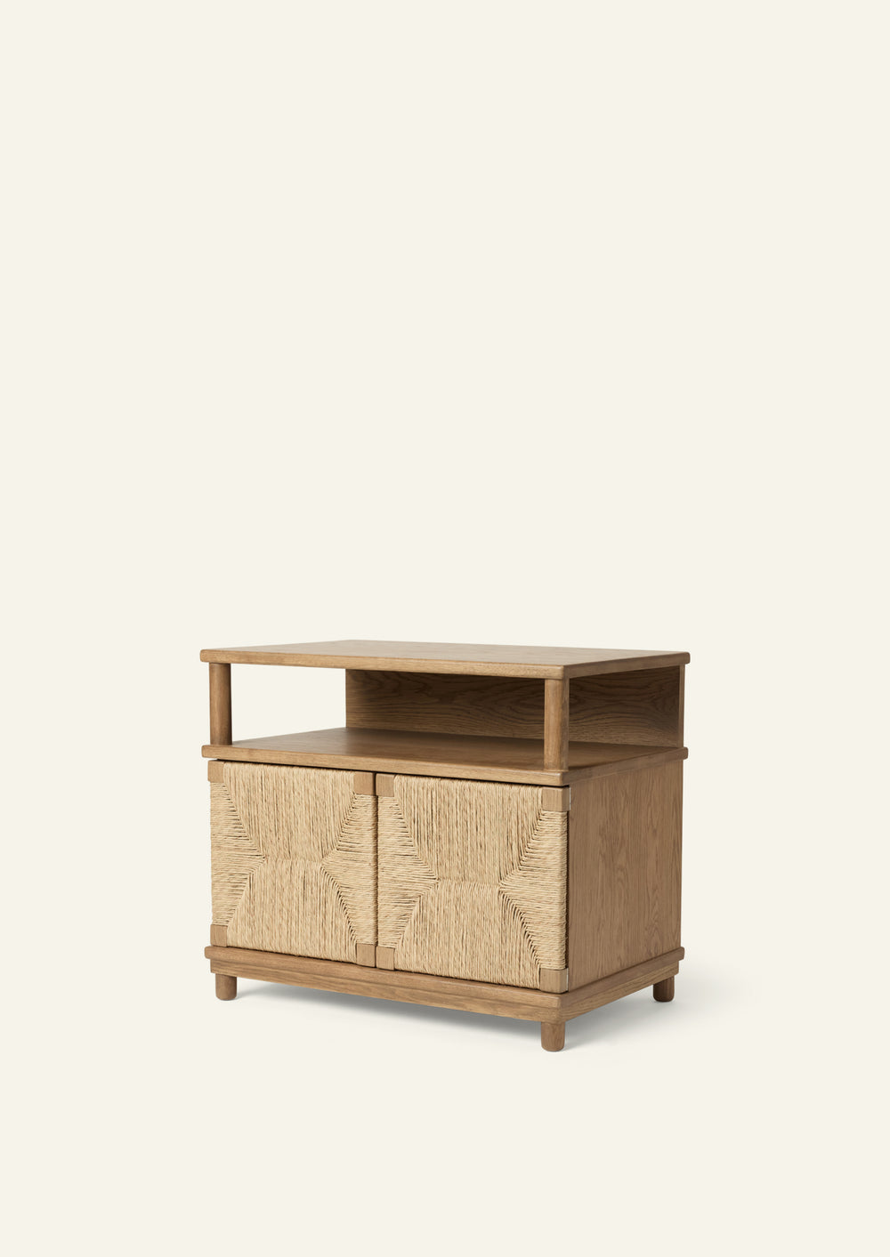 Three-quarter view of a nightstand crafted from solid honey oak with woven seagrass rush door fronts. An open upper shelf provides easy-access storage, while the textured doors add warmth and visual interest.