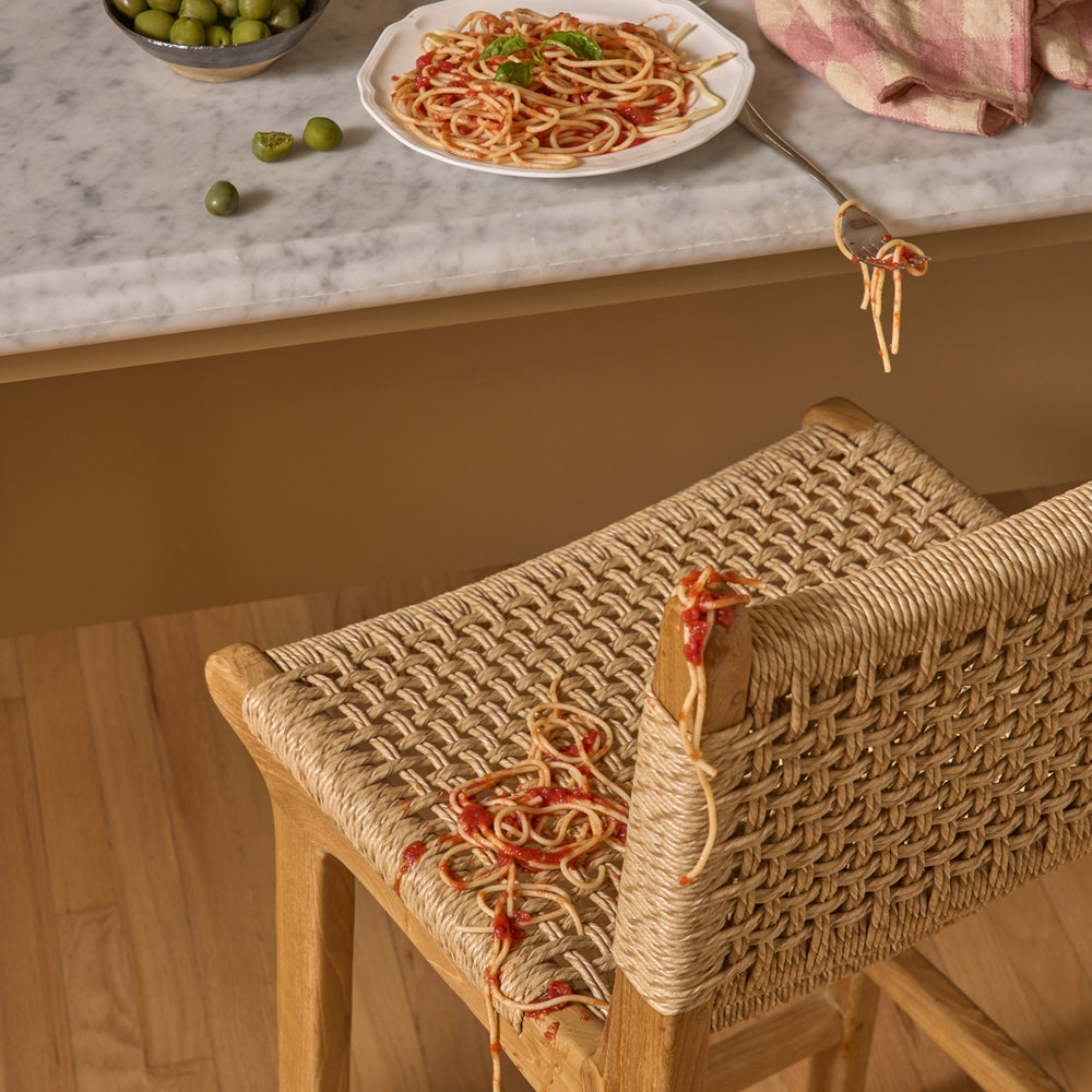 Synthetic Paper Cord Teak stool with spaghetti on a marble countertop with pasta and olives.