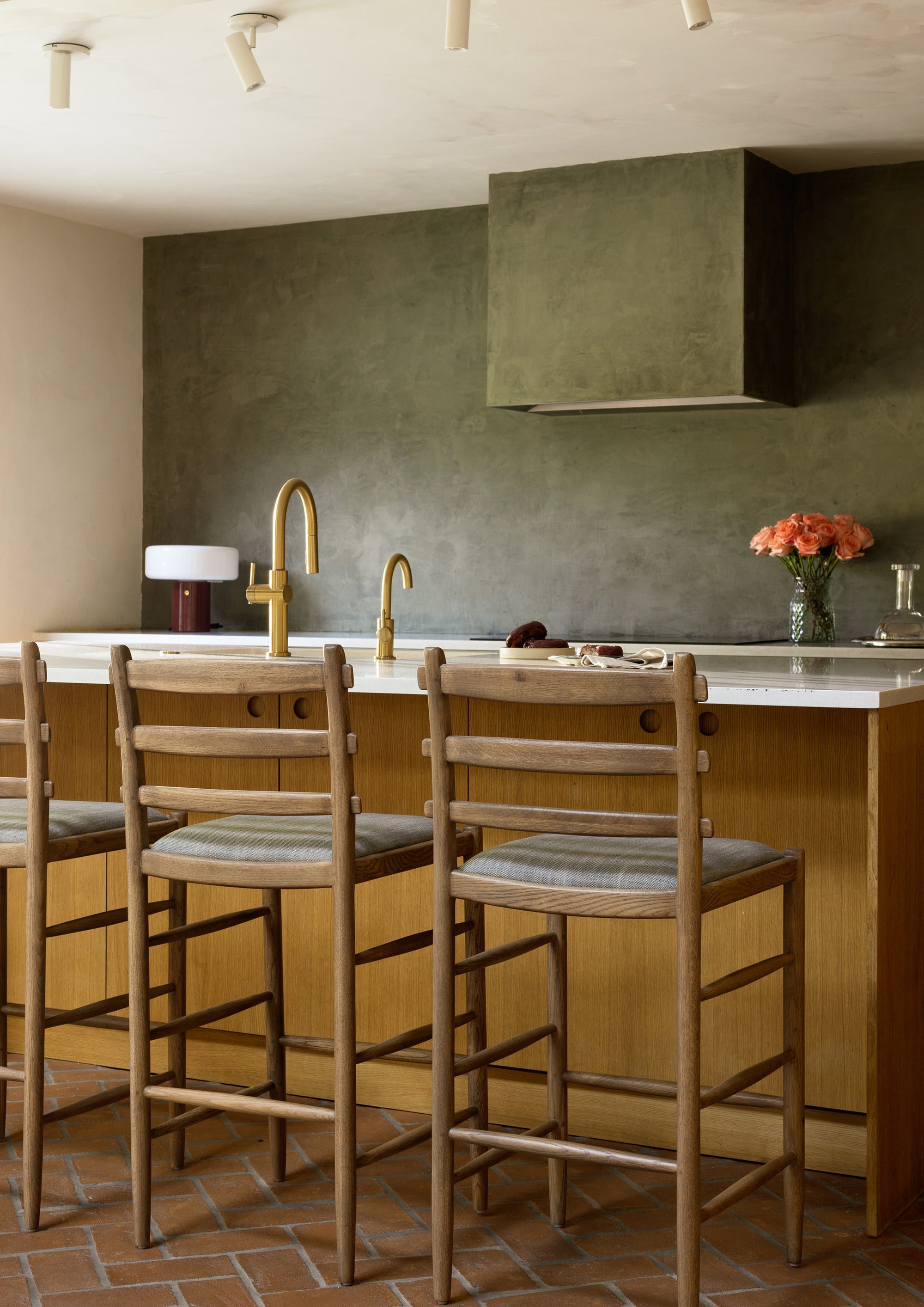 Modern green kitchen with Tiga honey oak counter stools, a blue-grey upholstered seat and various styled elements. 
