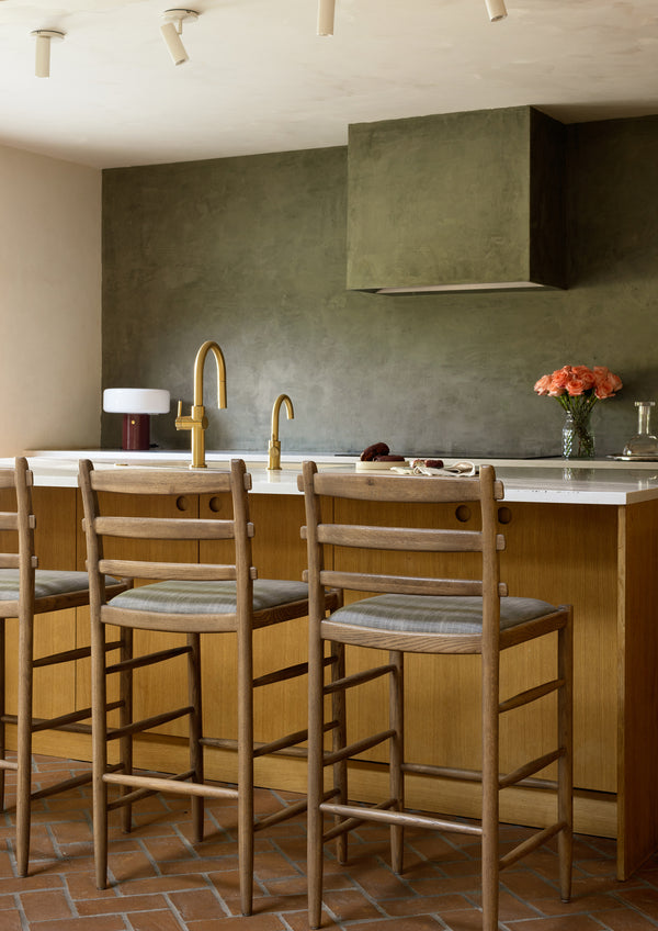 Modern green kitchen with Tiga honey oak counter stools, a blue-grey upholstered seat and various styled elements. 