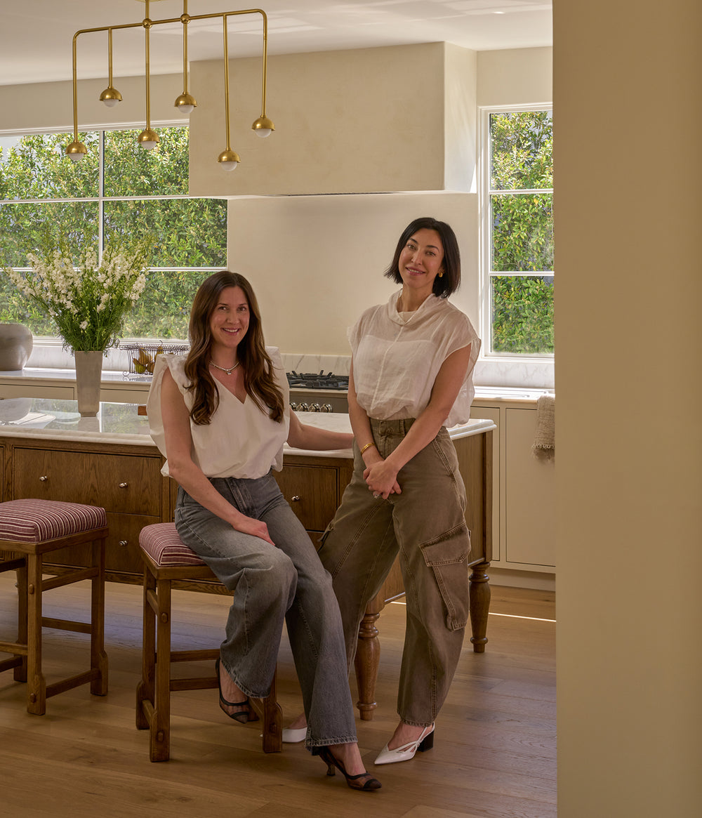 Two women sitting on Sari Counter Stools in a modern kitchen with large windows and a view of greenery.
