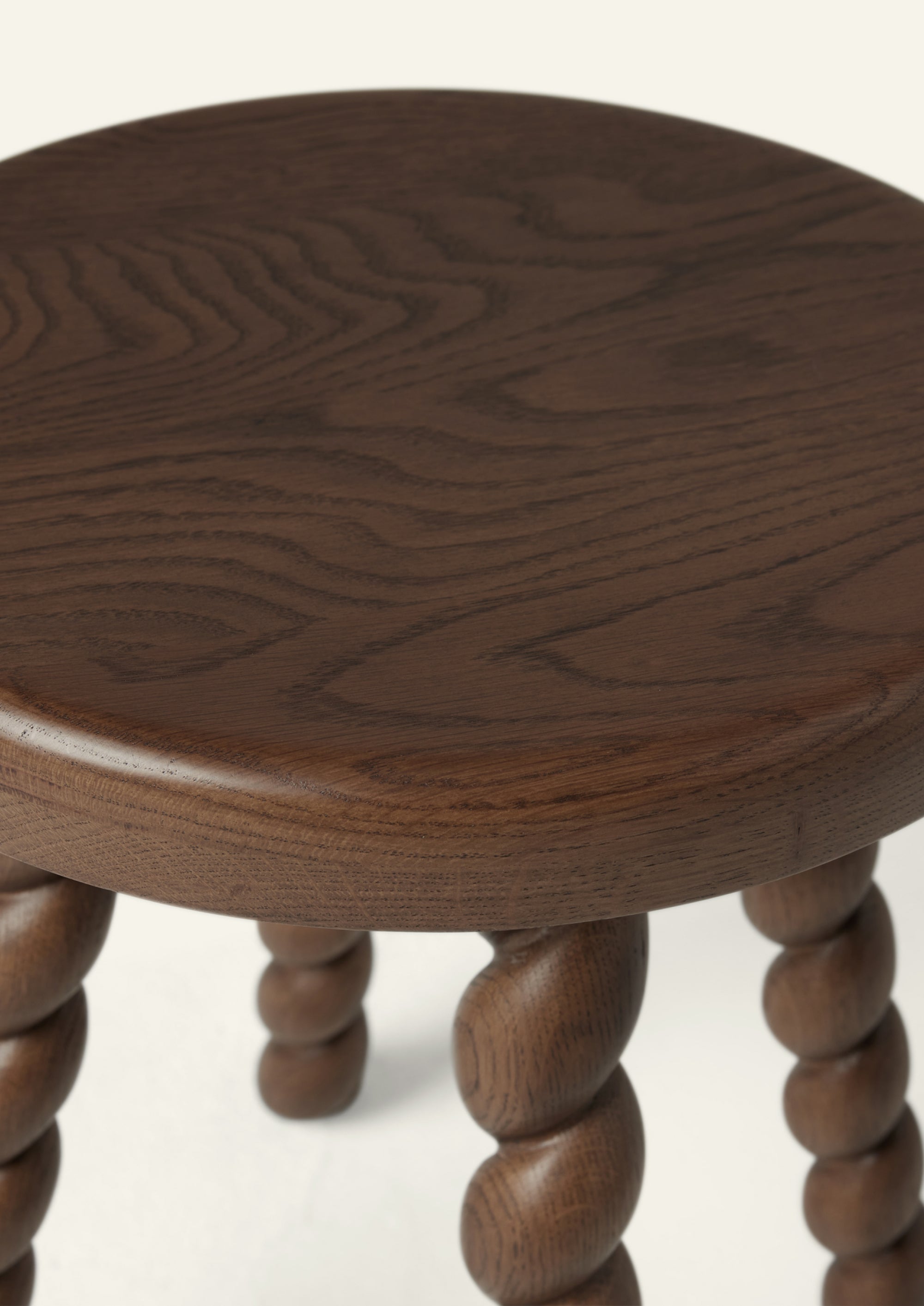 Close-up of the stool’s round oak top, showcasing the wood’s natural grain and warm brown finish. The gently rounded edge highlights the craftsmanship and soft, organic form.
