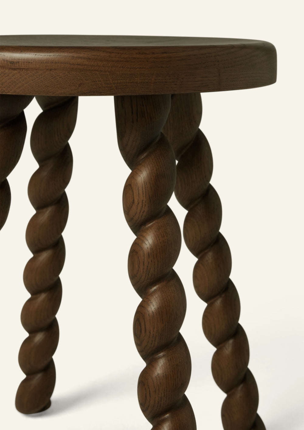 Close-up of the stool’s hand-finished spiral-turned oak legs, highlighting the sculptural detailing, rich brown tone, and visible wood grain.