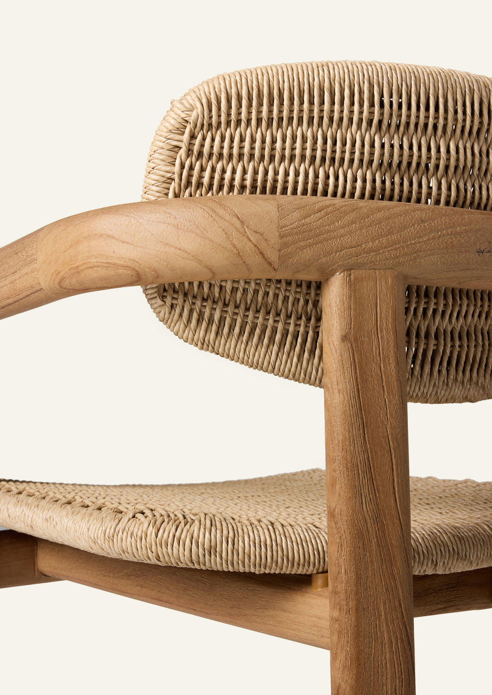 Close-up of the dining chair showcasing the solid teak armrest, natural wood grain variation, and handwoven synthetic paper cord backrest. The combination of warm materials and rounded forms highlights the chair’s craftsmanship.