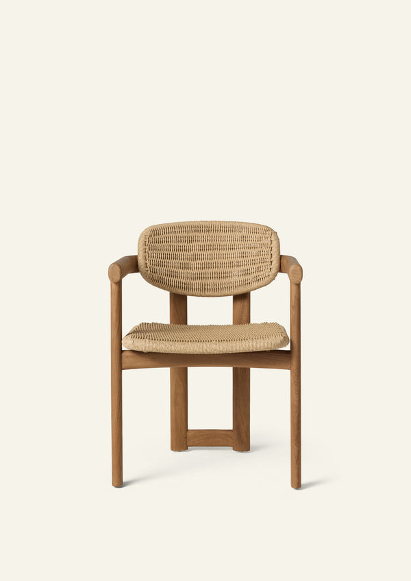 Front view of the dining armchair featuring a woven synthetic paper cord seat and backrest framed by solid teak arms and legs. The generous proportions and rounded forms provide both comfort and visual warmth.