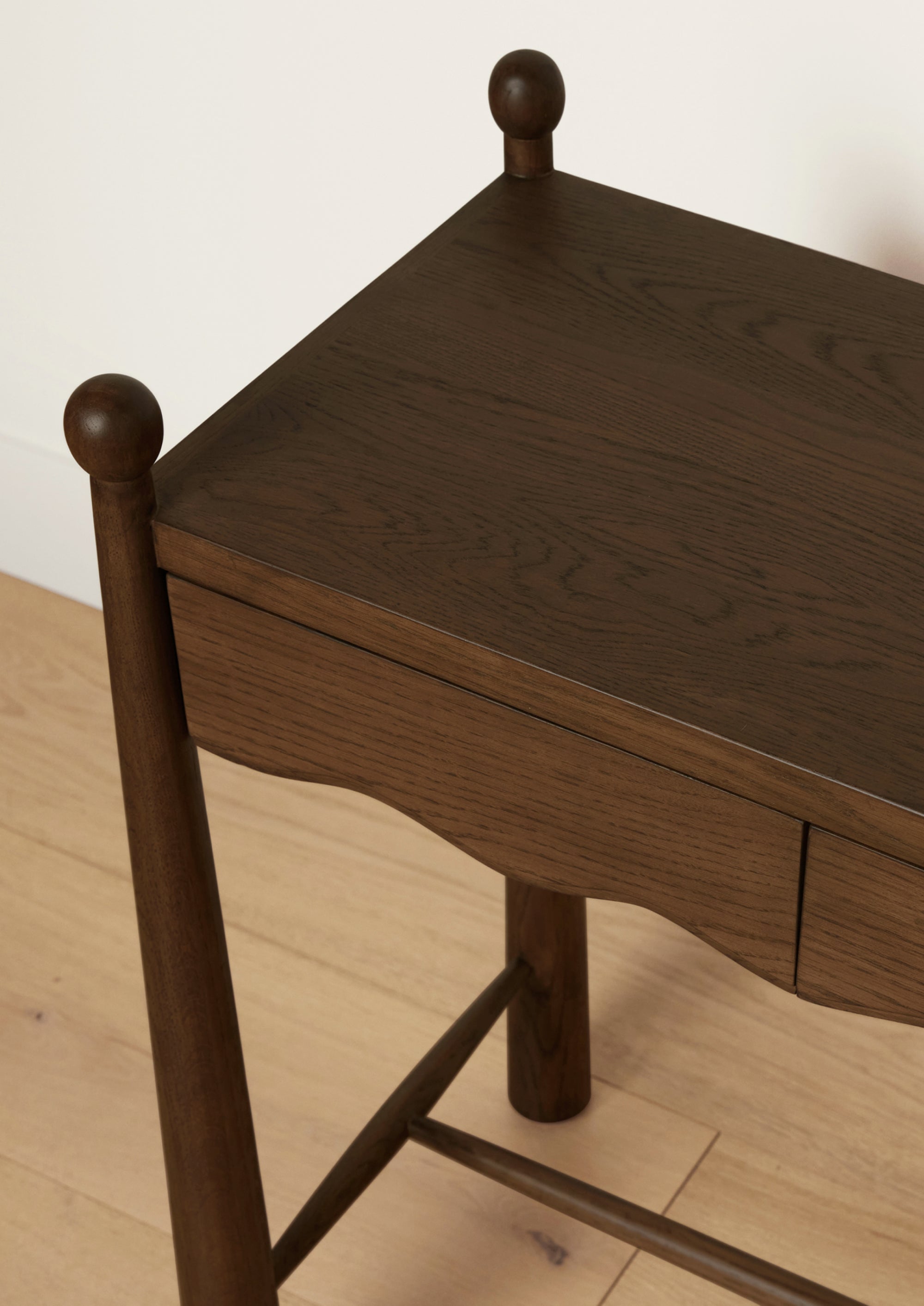 Close-up of a dark oak console table highlighting the rich wood grain, rounded finials, and softly scalloped apron. 