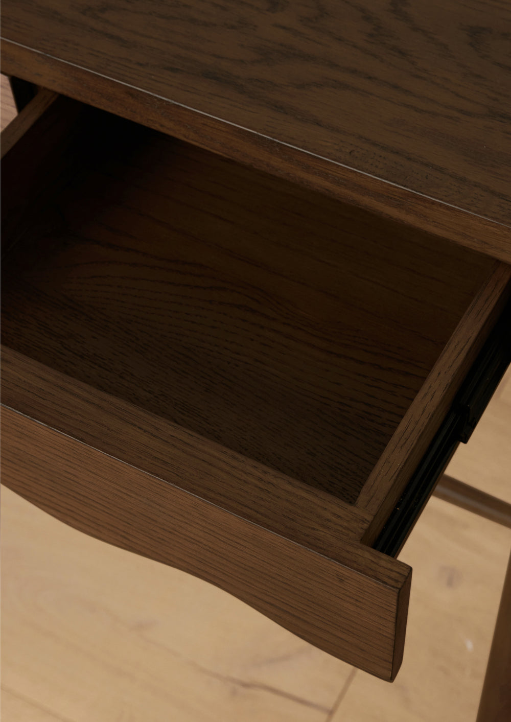 Close-up of an open drawer in a dark oak console table, showcasing the spacious wood interior, rich grain pattern, and scalloped drawer front detail.
