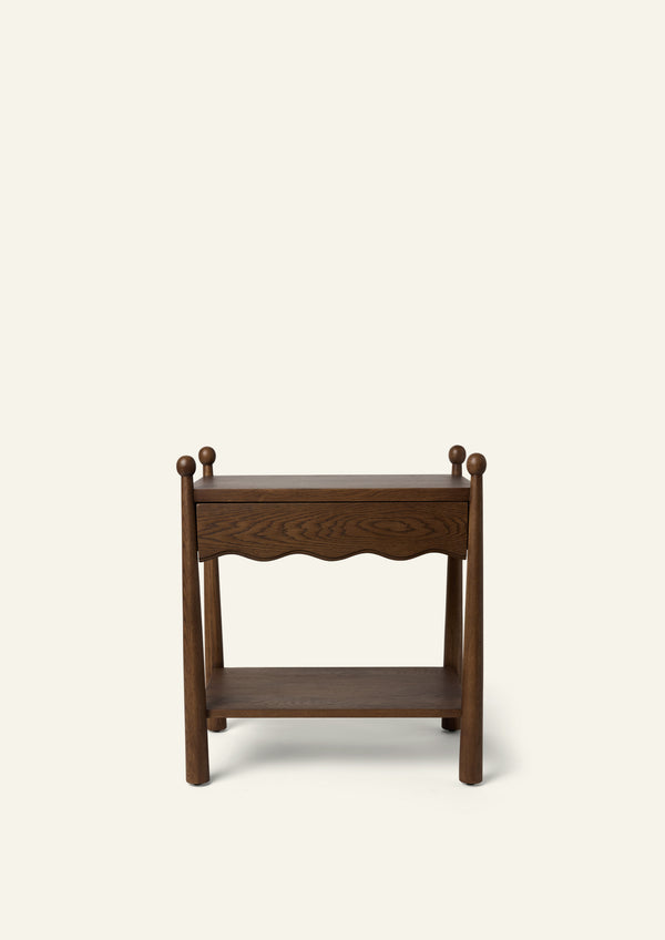 Front view of a dark oak nightstand featuring a single drawer with a scalloped apron, rounded finials, and an open lower shelf for additional storage. Photographed against a soft ivory background.