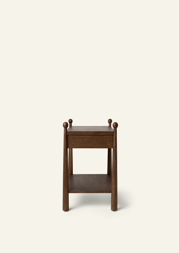 Side profile of a dark oak nightstand featuring a single drawer, open lower shelf, tapered cylindrical legs, and rounded finials. The clean silhouette highlights the balance between traditional detailing and functional storage.