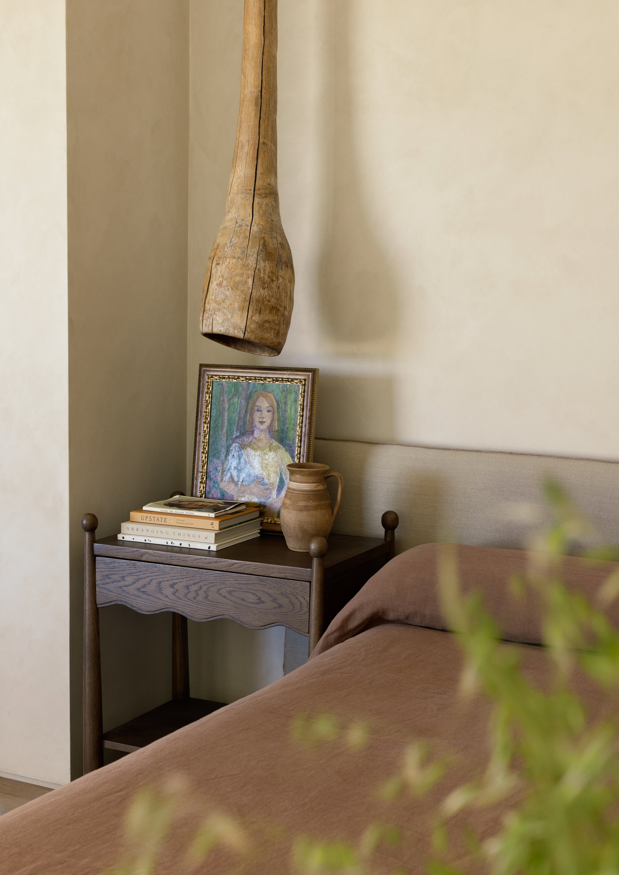 A warm, desert style bedroom with the Wave brown oak nightstand featuring a painting and books, and a decorative vase on a neutral wall.