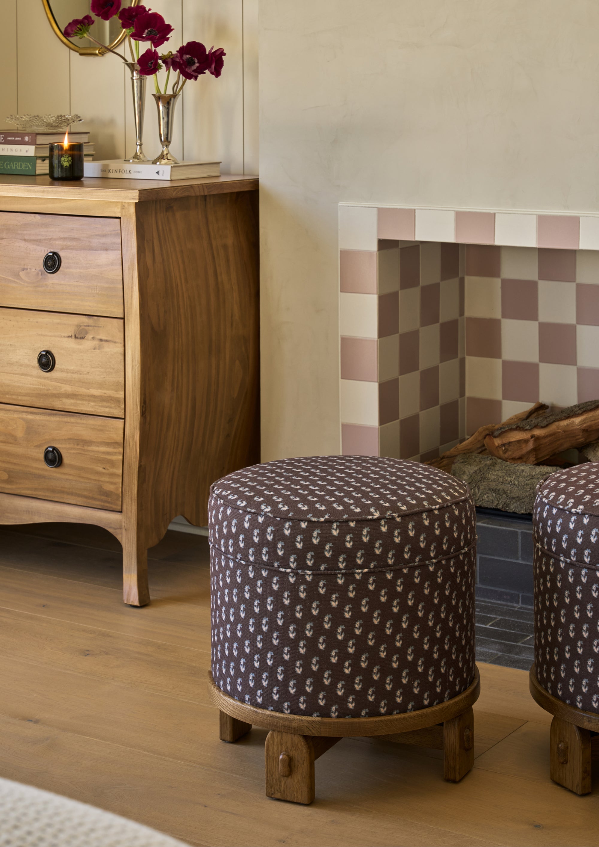 Two Yara Poufs in Cocoa Floral are styled beside a fireplace in a warm, inviting living space. The patterned upholstered poufs add extra seating while introducing color, texture, and a playful vintage-inspired accent.