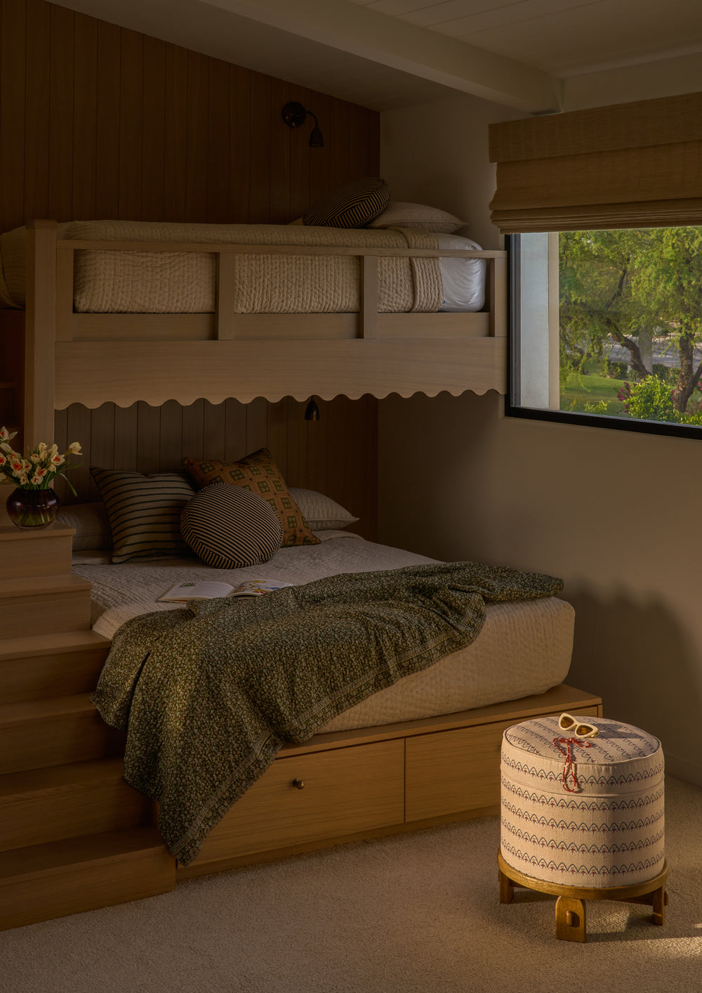 The Cleobella Yara Pouf in Neutral Arches sits beside a built-in bunk bed in a warmly lit bedroom. The upholstered pouf adds playful pattern and versatile seating to the cozy, family-friendly space.