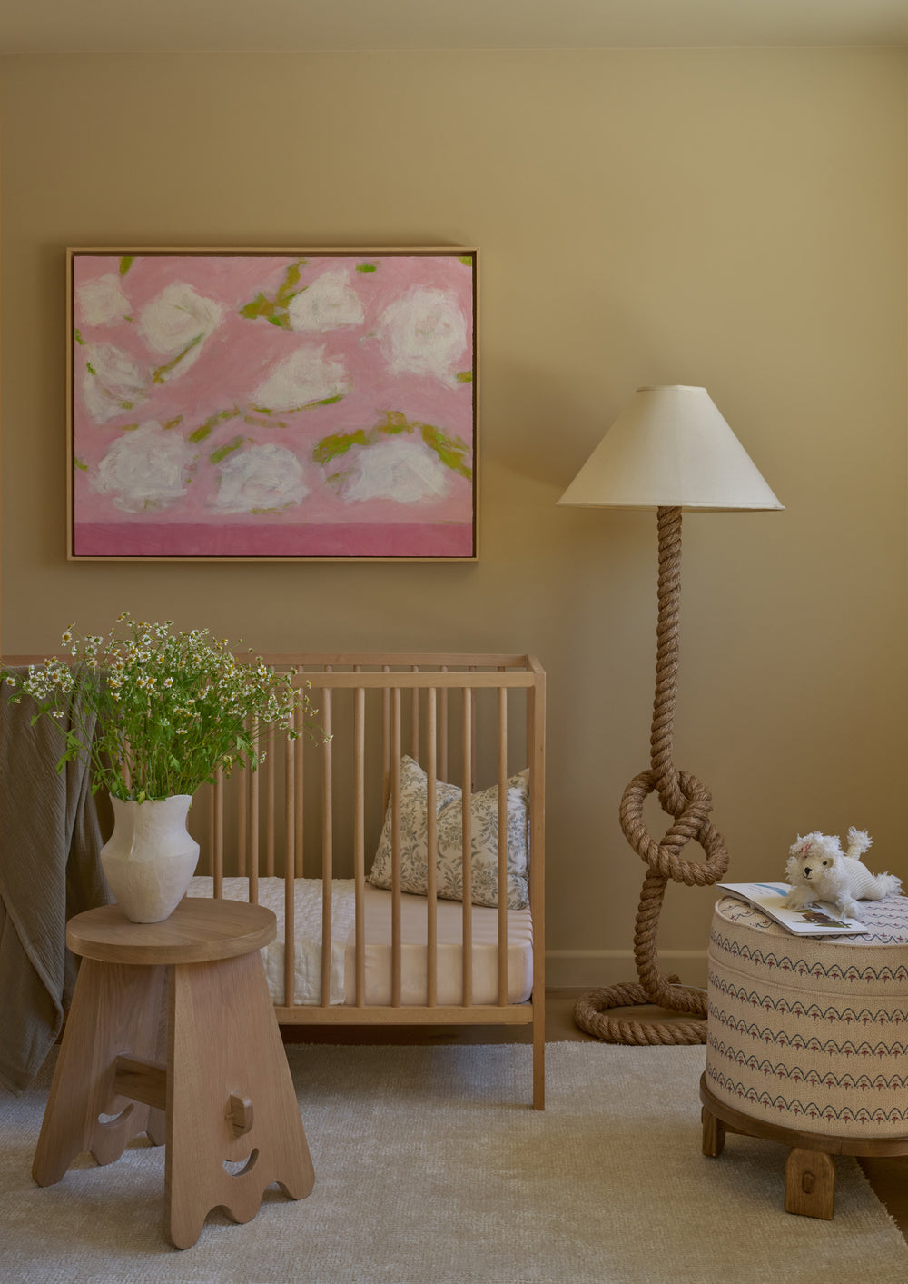 The Yara Pouf in Neutral Arches is styled in a nursery beside a light oak crib and sculptural rope floor lamp. The soft patterned upholstery adds warmth, texture, and whimsy to the room.