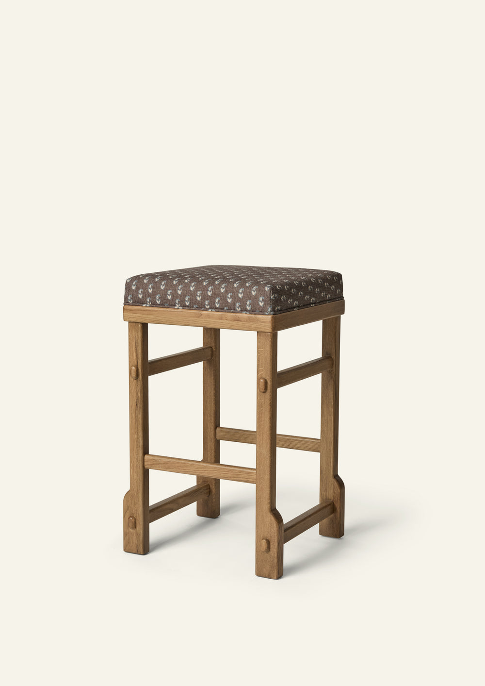 Upholstered counter stool featuring Cocoa Floral fabric atop a solid honey oak frame. The tailored silhouette combines a delicate floral motif with warm wood tones and traditional joinery details.