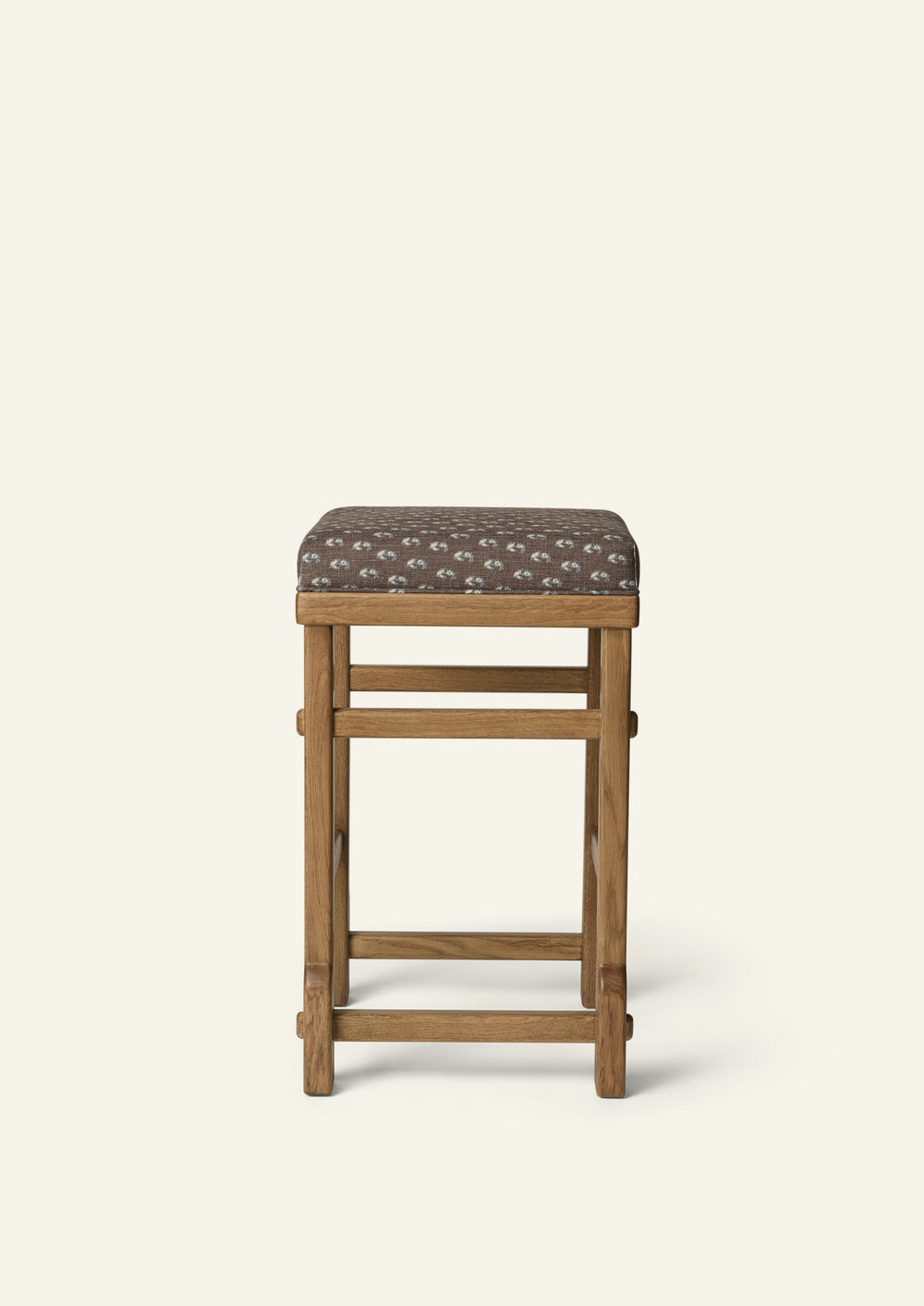front view of an upholstered counter stool with Cocoa Floral fabric and a solid honey oak frame. Clean lines and handcrafted joinery create a timeless, versatile design.