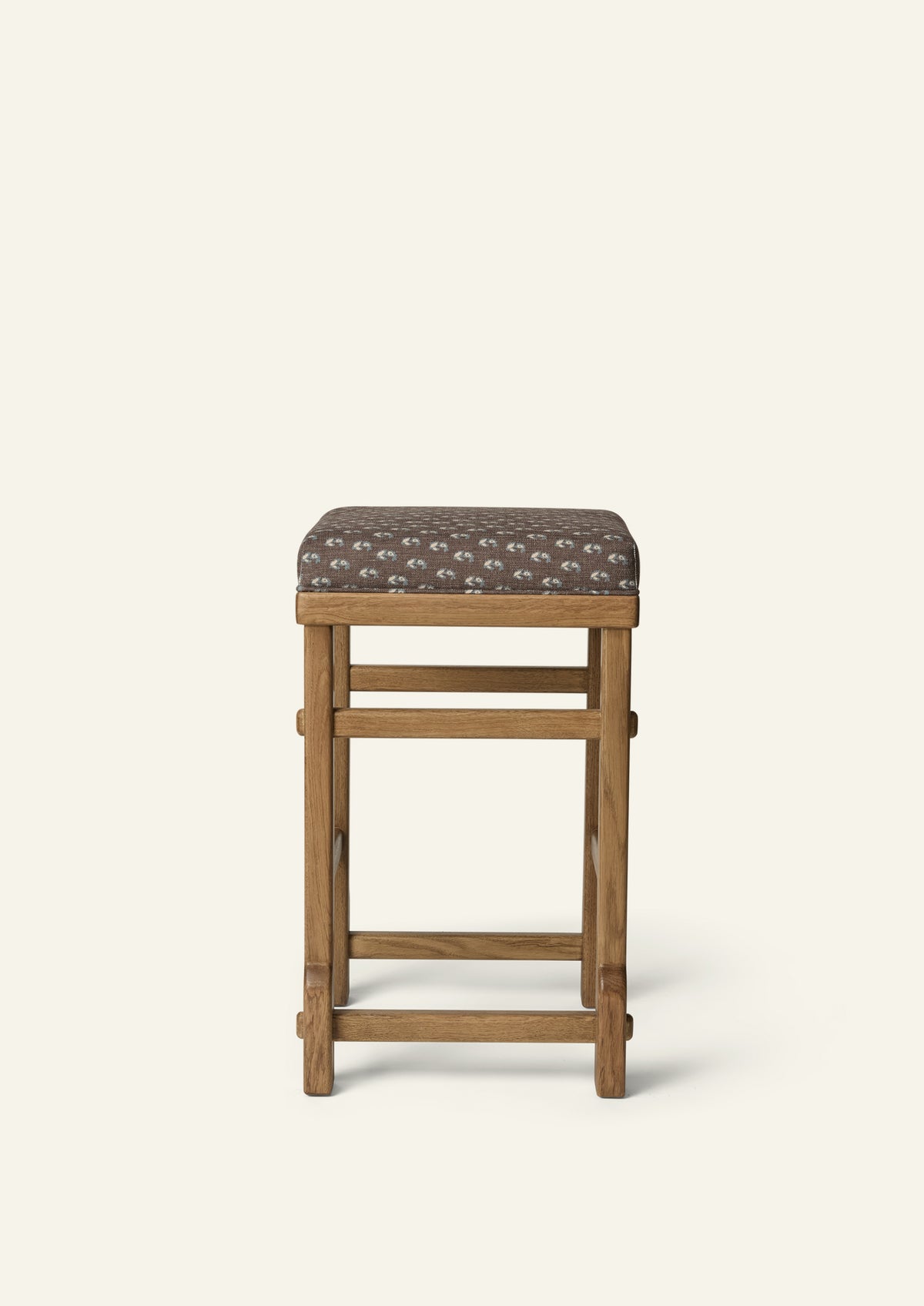 front view of an upholstered counter stool with Cocoa Floral fabric and a solid honey oak frame. Clean lines and handcrafted joinery create a timeless, versatile design.