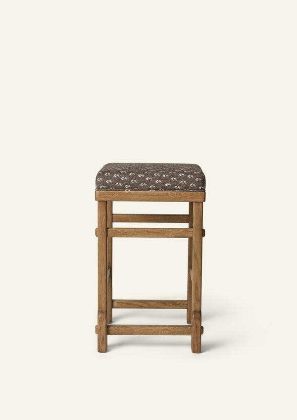 front view of an upholstered counter stool with Cocoa Floral fabric and a solid honey oak frame. Clean lines and handcrafted joinery create a timeless, versatile design.
