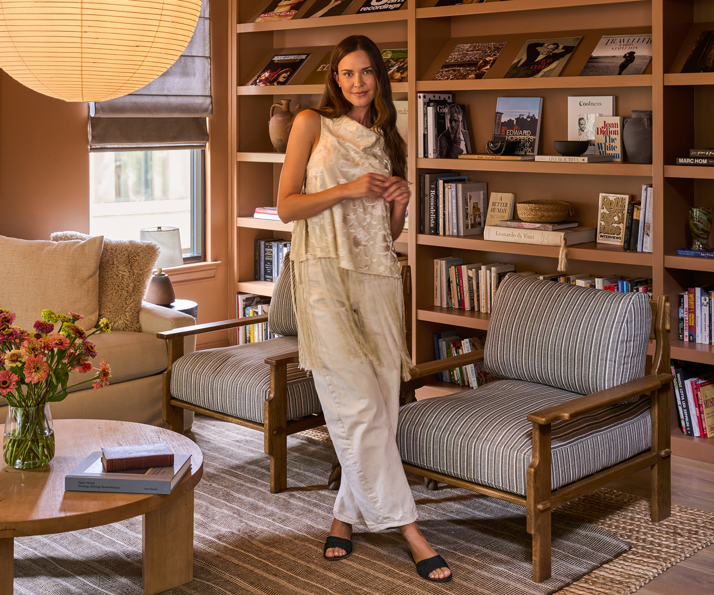 Odette Annable standing in a cozy living room with bookshelves and furniture.