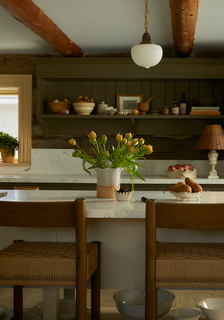 Kitchen with wooden chairs, white countertop, and shelves with decorative items.