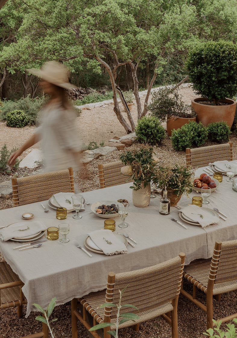 Outdoor dining setup with a person in a hat walking by, surrounded by greenery.