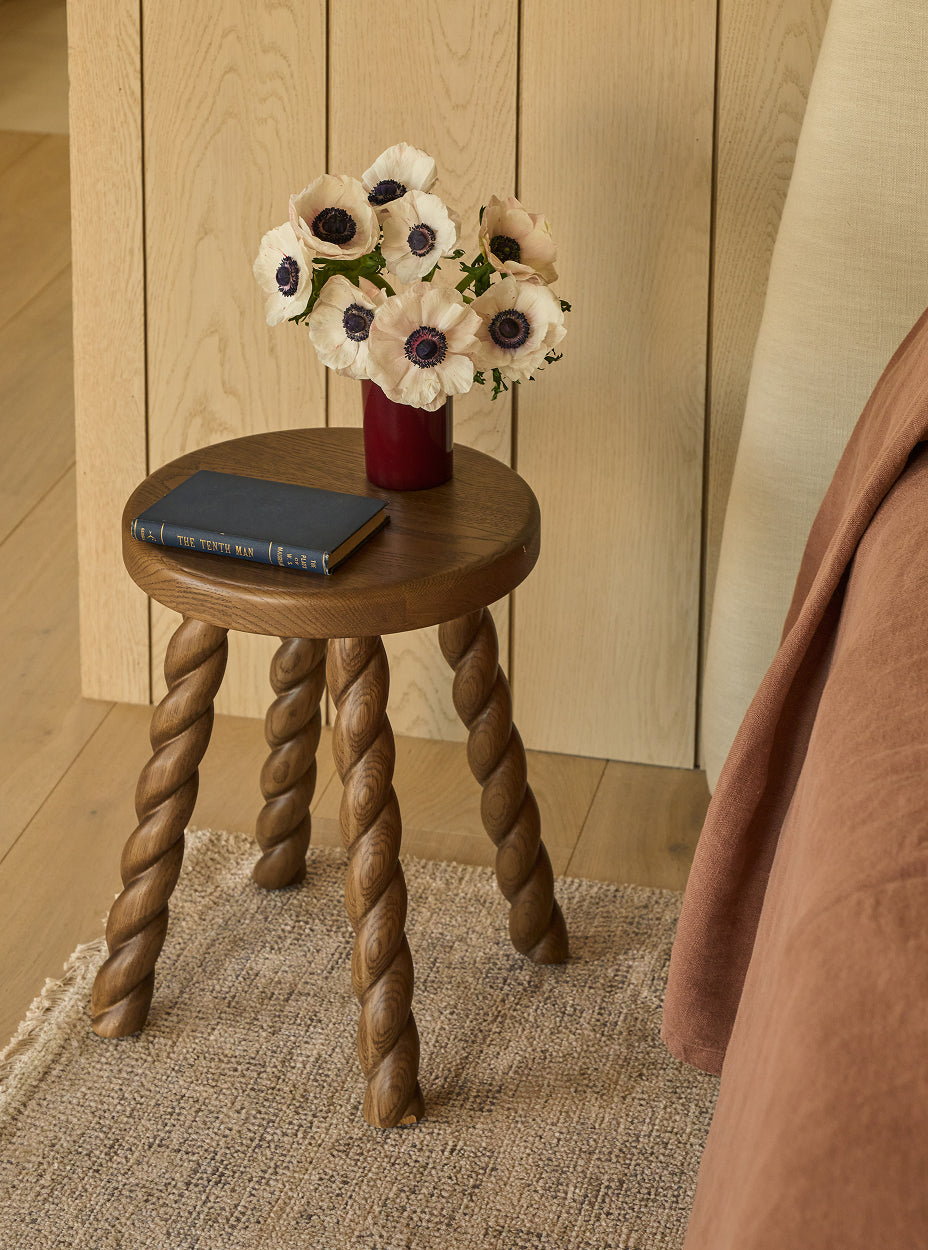 Twist side table with twisted legs holding a vase of flowers and a book against a wooden wall.