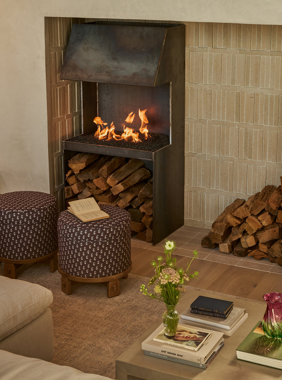 Living room with a fireplace, yara poufs, and a coffee table with books and a vase.