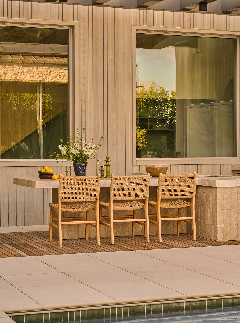 Outdoor dining area with bali dining chairs and a table near a poolside.