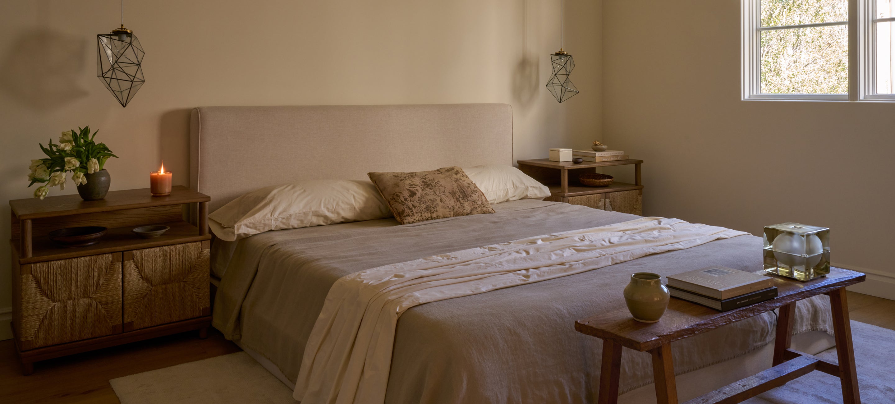 Neatly made bed in a bedroom with a side table and window.