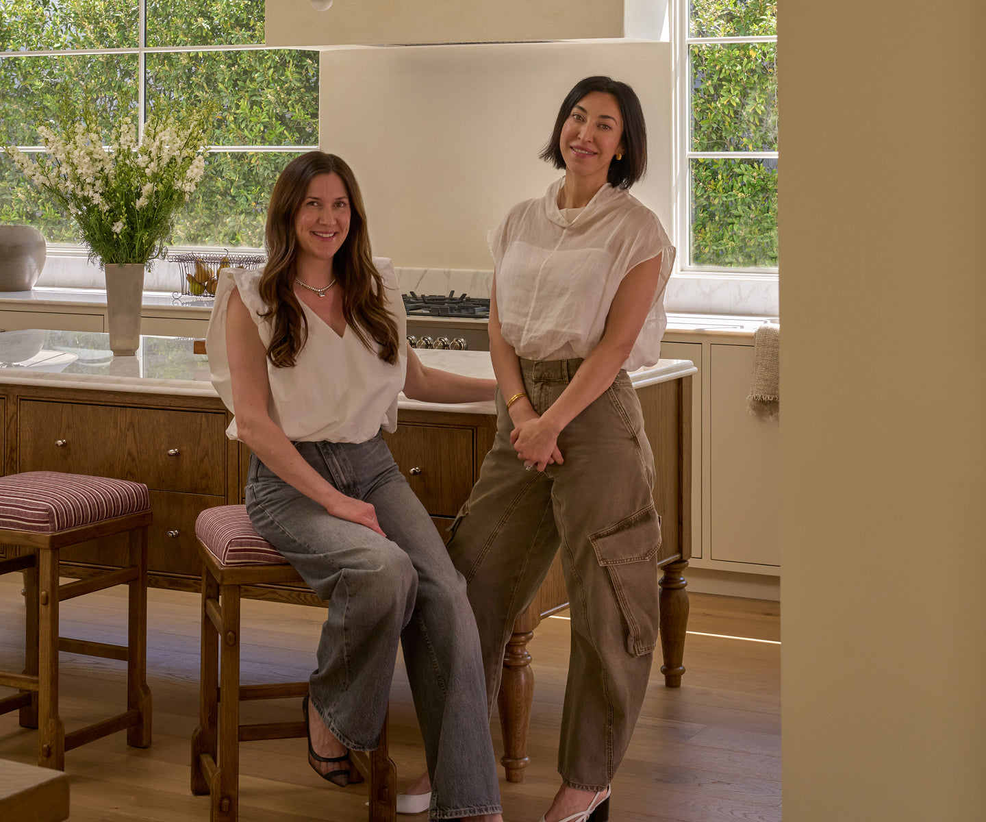 Two women posing in a kitchen with a window in the background