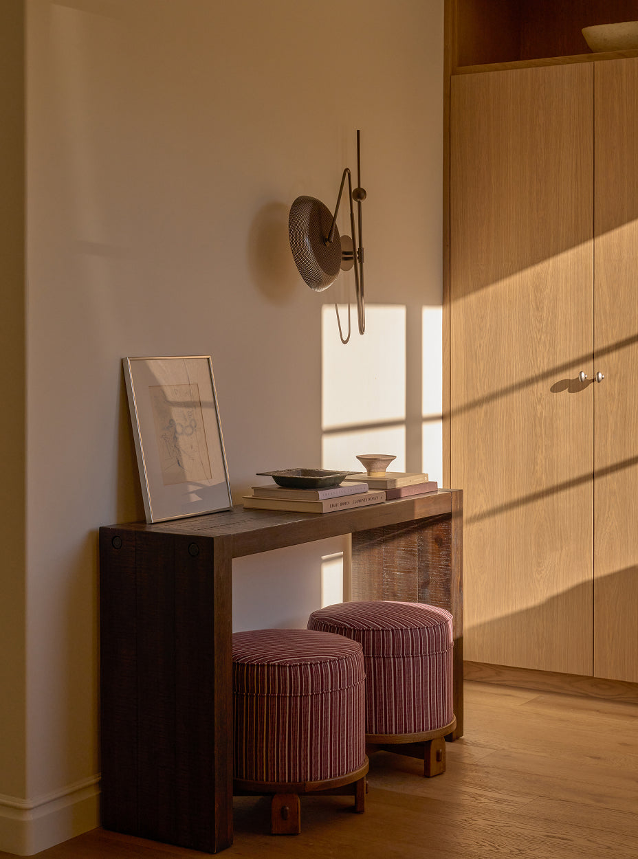 Small wooden console table with books and a bowl against a wall, with two yara poufs in front.