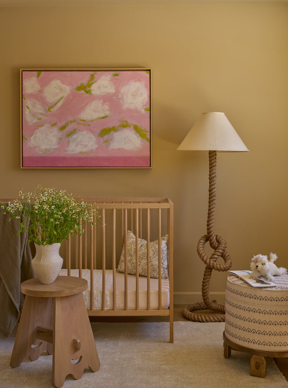 Nursery room with wooden crib, pink floral artwork, the senja side table, and the yara pouf.