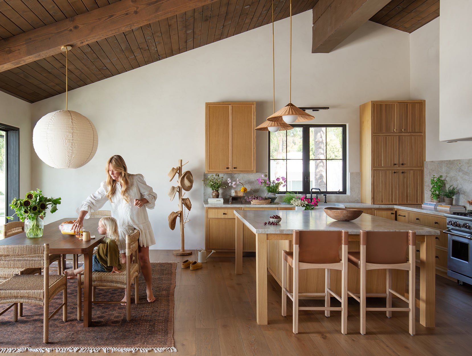 Modern kitchen with wooden cabinets and  Henrik counter stools, Grace standing near the dining table with Suma chairs.