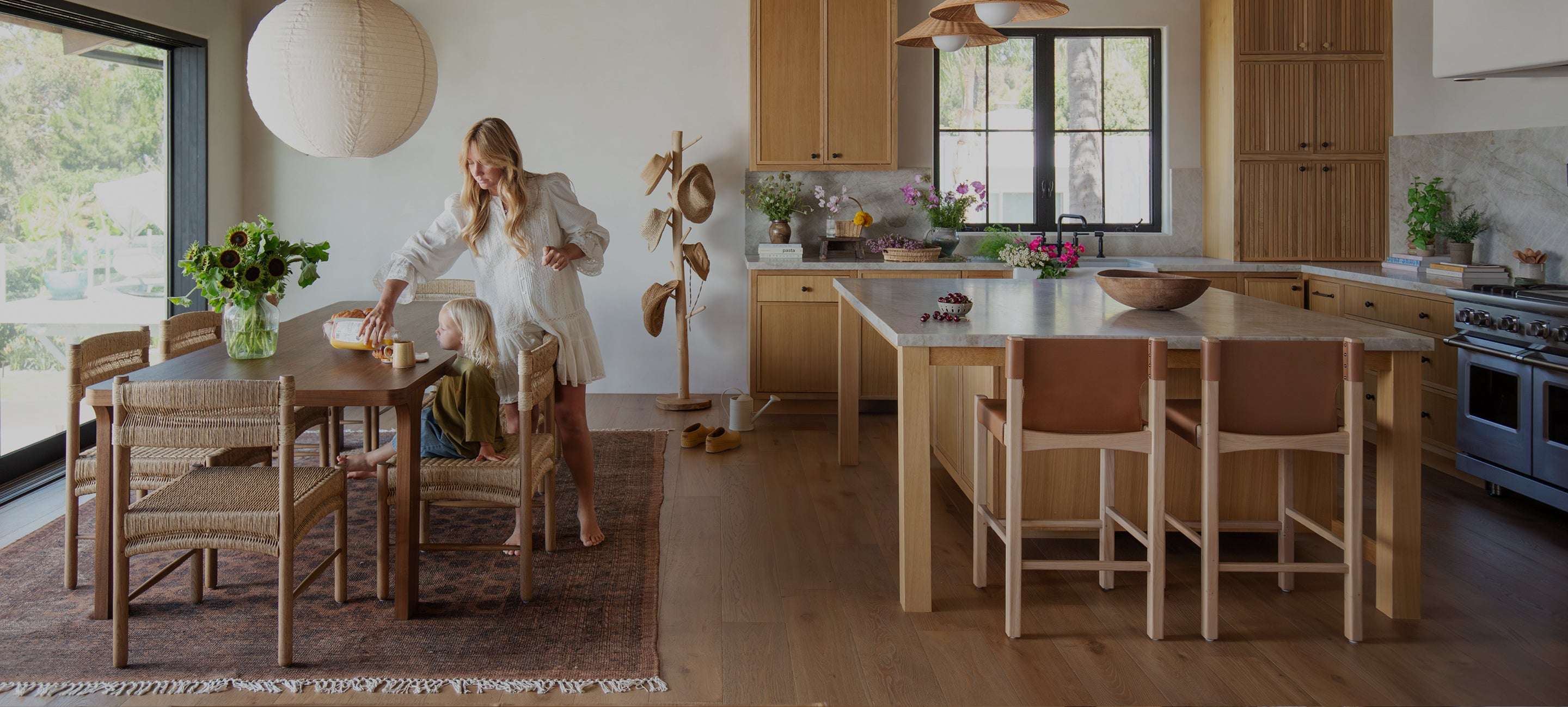 Woman in a modern kitchen with wooden furniture and large windows.