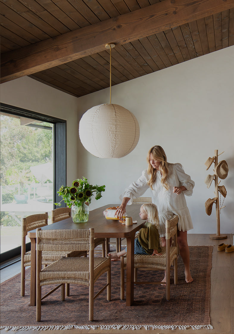 Woman and child at a wooden dining table in a modern home with large windows.