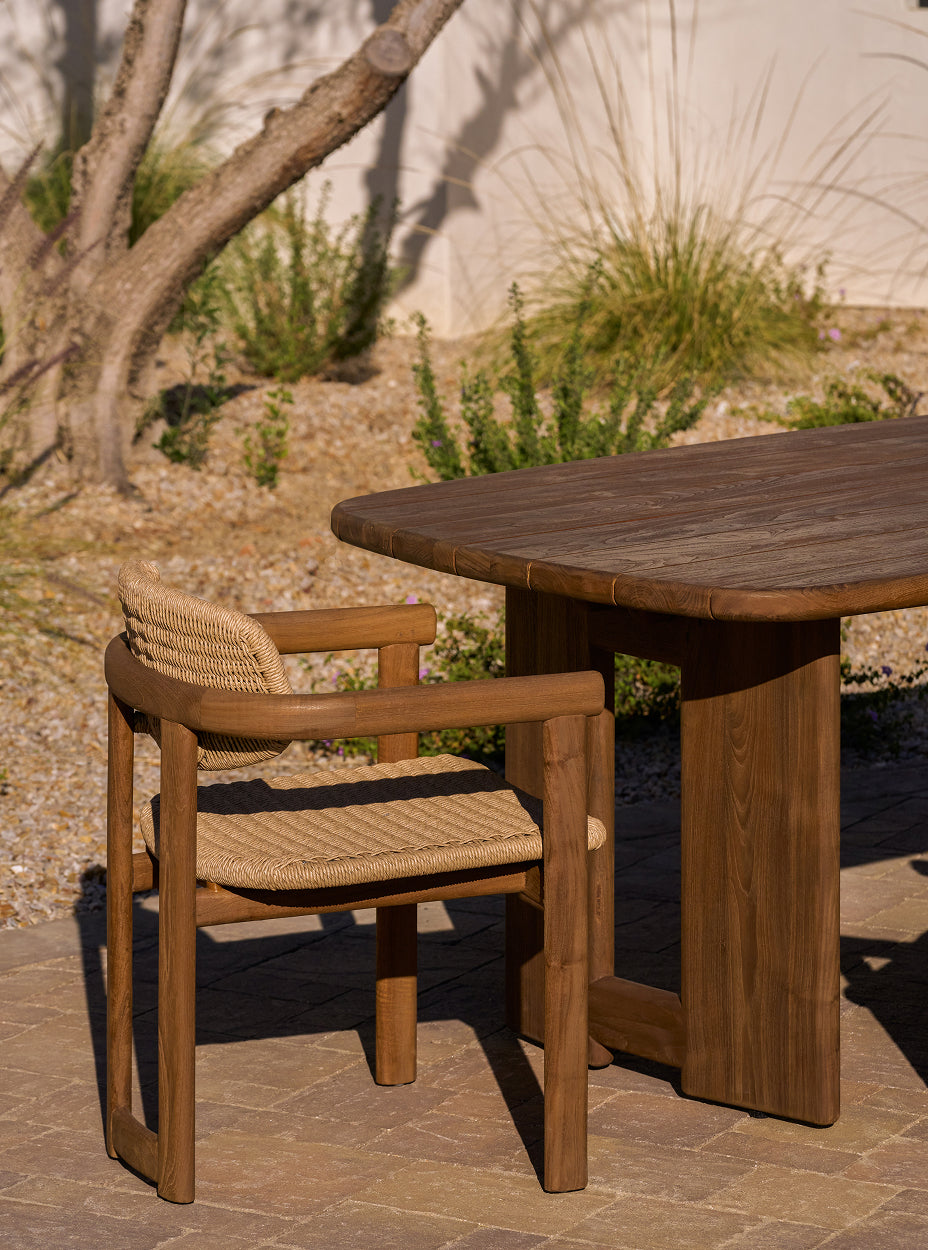 Outdoor setting with the hollis dining table and the vera dining chairs under a tree in front of a stone building.