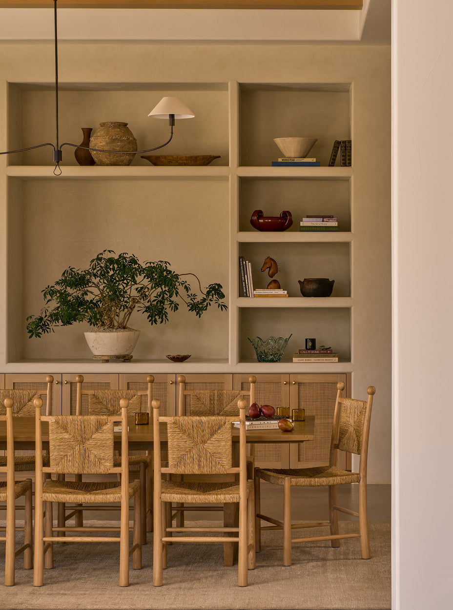 Dining area with wooden table and chairs in front of a wall with open shelves.