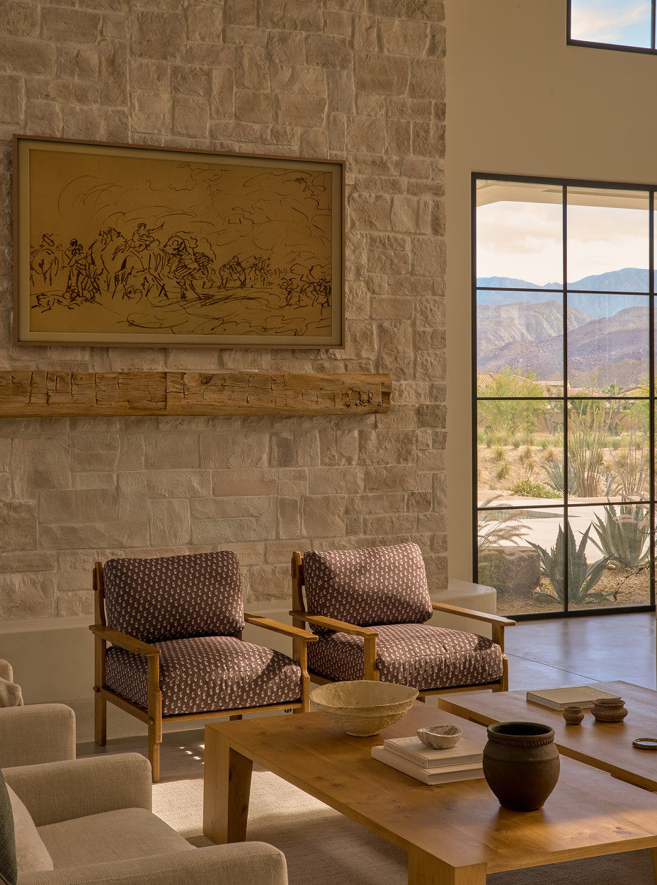Living room with stone wall, framed artwork, two leela lounge chairs, and a large window view.