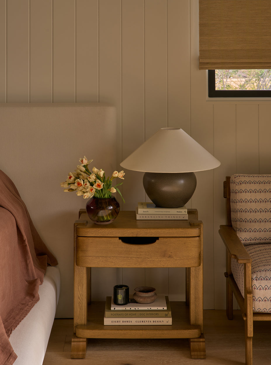 The mina nightstand with lamp, books, and vase in a bedroom setting